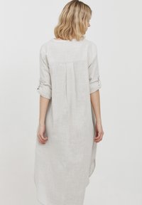 Hellgraues Leinenkleid mit lockerer Passform, mit umgeschlagenen Ärmeln und einem Rückenschlitz für zusätzliche Bewegungsfreiheit. Einfaches, strukturiertes Stoffdesign.