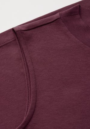 Burgundy tričko s jemnou texturou, kulatým výstřihem a krátkými rukávy. Viditelné prošívané švy podél límce a ramen.