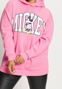 Sudadera rosa con un gran texto "MICKEY" y un gráfico de Mickey Mouse. Presenta un corte relajado y puños y dobladillo acanalados.