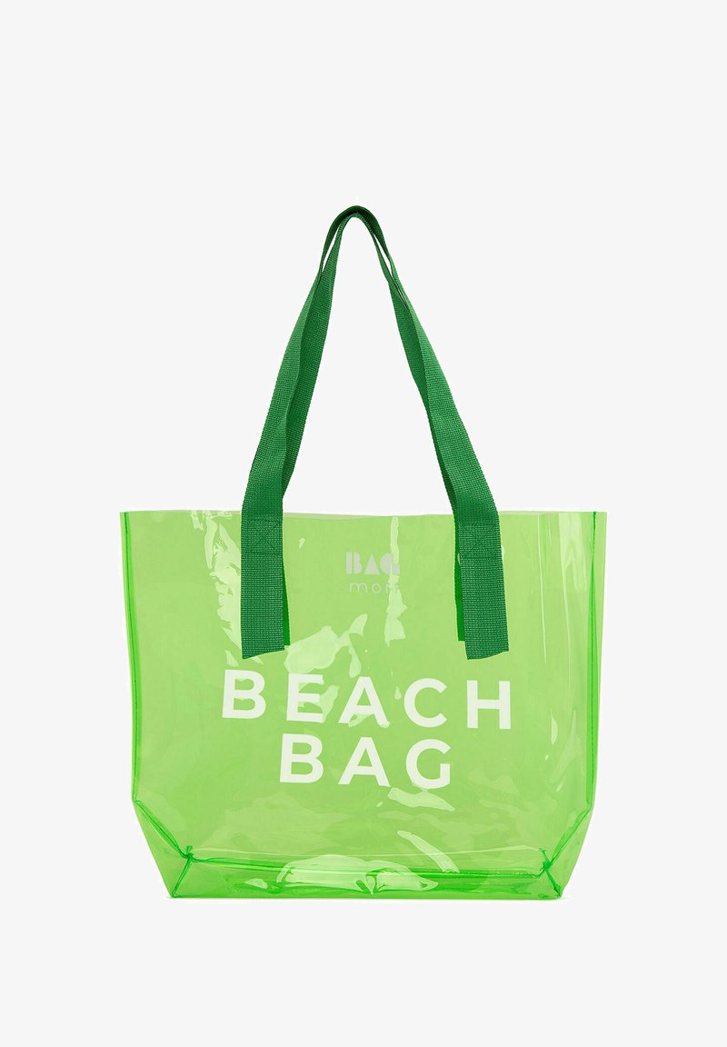 Caurspīdīga zaļa pludmales soma ar baltu tekstu "PLUDMALES SOMA", aprīkota ar izturīgām zaļām rokturiem un taisnstūra formu. Mīksta plastmasas materiāls.