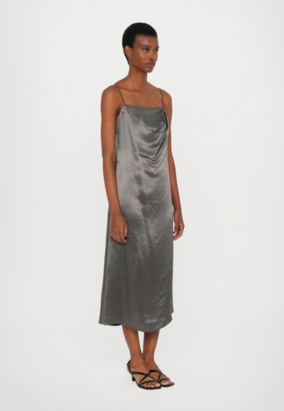 Satin gray slip dress with a cowl neckline and thin straps, falling to mid-calf. Worn with black strappy sandals. Smooth texture.
