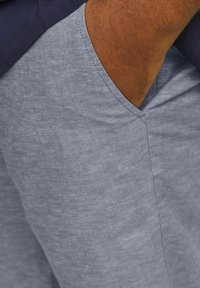 Shorts en lin gris clair avec un détail de poche en forme de V. Présente un tissu texturé et des coutures nettes. Portés avec un haut navy.