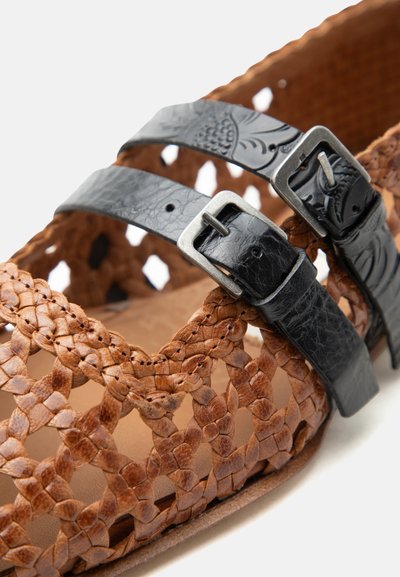 Καφέ πλεκτό δερμάτινο σανδάλι με δύο μαύρες ανάγλυφες δερμάτινες λουρίδες και μεταλλικές αγκράφες στην κορυφή.