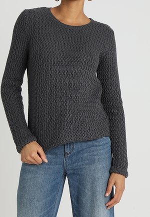 Pull en maille gris foncé avec un motif texturé de type gaufre. Manches longues et encolure ronde, associé à un jean en denim clair.