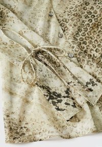 Blusa leggera color beige con stampa animale testurizzata. Presenta chiusura con bottoni e un dettaglio a fiocco sul lato. Tessuto morbido e fluido.