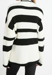 Übergroßer Strickpullover mit auffälligen schwarz-weißen Streifen, geripptem Textur, weiten Ärmeln und hohem Halsausschnitt.