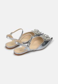 Zapatos planos de tira metálica plateada con punteras puntiagudas, adornados con acentos florales de strass, y un interior de cuero suave.