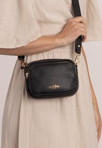 Schwarze Leder-Crossbody-Tasche mit goldenen Beschlägen, rechteckiger Form, Reißverschluss-Verschlüssen und geprägtem Markenlogo auf der Vorderseite. Texturierte Oberfläche.