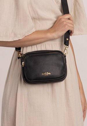 Black leather crossbody bag with gold hardware, rectangular shape, zip closures, and embossed brand logo on the front. Textured finish.