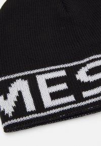 Beanie en tricot noir avec du texte blanc contrastant. Présente une texture côtelée et un bord replié, offrant un ajustement serré.