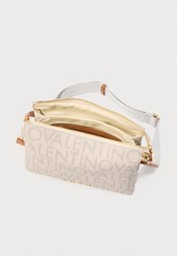 Bež Valentino torbica na remenu s zlatnim patentnim zatvaračima, trakastim remenom s logotipom od tkanine i više pretinaca otvorena kako bi se pokazala svijetla unutarnja podstava.