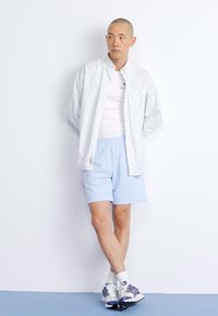 Lysblå shorts, hvid tanktop og en stribet skjorte med knapper. Hvide sneakers med lilla accenter. Glat stof og afslappet pasform.