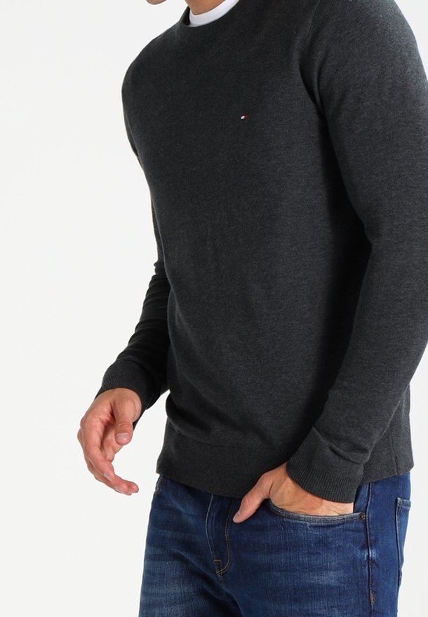 Pull ras du cou gris foncé en tissu doux ; présente des poignets et un ourlet côtelés, avec un petit logo sur la poitrine. Associé à un jean bleu.