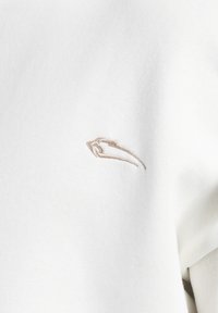 Tessuto bianco con un piccolo logo in rilievo marrone, che presenta una texture liscia con una leggera lucentezza.