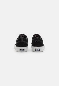 Baskets en suède noir avec semelles en caoutchouc blanc, présentant un design cousu, un bout arrondi et un logo iconique sur le talon.