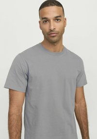 Camiseta de manga corta gris hecha de algodón suave. Presenta un cuello redondo y un diseño simple y liso, sin patrones ni detalles.