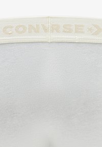 Balts kokvilnas sajaukuma tops ar ribotu faktūru un krēmkrāsas elastīgu vidukļa joslu ar izceltiem burtiem "CONVERSE".