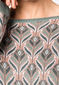 Gebreide pullover met een zacht perzik- en groentintenschema, met een geometrisch bladerenpatroon in wit en donkergroen. Brede halslijn.