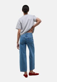 T-shirt gris à manches courtes, jeans taille haute bleu clair et ballerines rouges. Les jeans ont des poches arrière et une coupe décontractée, large.