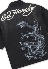 Schwarze Jeansjacke mit weißem "Ed Hardy"-Schriftzug oberhalb einer großen, detaillierten silbernen Drachengrafik auf der Rückseite.