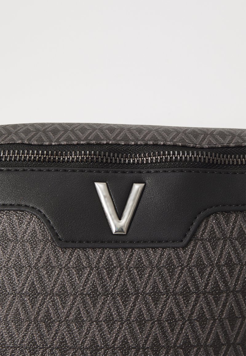 Sac gris texturé avec un motif en diamant, des accents en cuir noir et un logo "V" argenté. Fermeture éclair en haut.