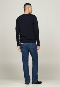 Marineblauer Pullover mit langen Ärmeln, gerippten Bündchen und Saum, getragen mit blauen, geraden Jeans, aus der Rückansicht gezeigt. Schlichtes und sauberes Design.