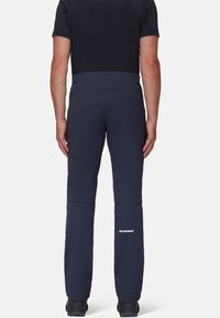 Marine softshell broek met een gladde textuur, met ritszakken en een wit logo op het onderbeen. Ontworpen voor buitenactiviteiten.