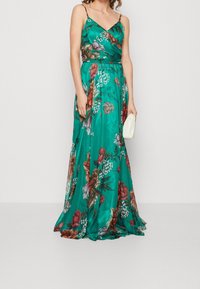 Long, teal floral dress made of satin with a wrap design, featuring colorful flowers, adjustable spaghetti straps, and a flowing hemline.