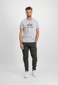 Graues T-Shirt mit bedrucktem Logo, karierte Hose in Dunkelgrün und weiße Sneaker. Die Cargo-Hose verfügt über mehrere Seitentaschen und eine taillierte Passform.