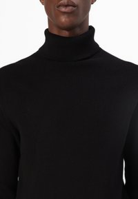 Fekete bordás garbó pulóver, puha anyagból készült, magas gallérral és testhezálló fazonnal, sima textúrával és minimalista stílussal.