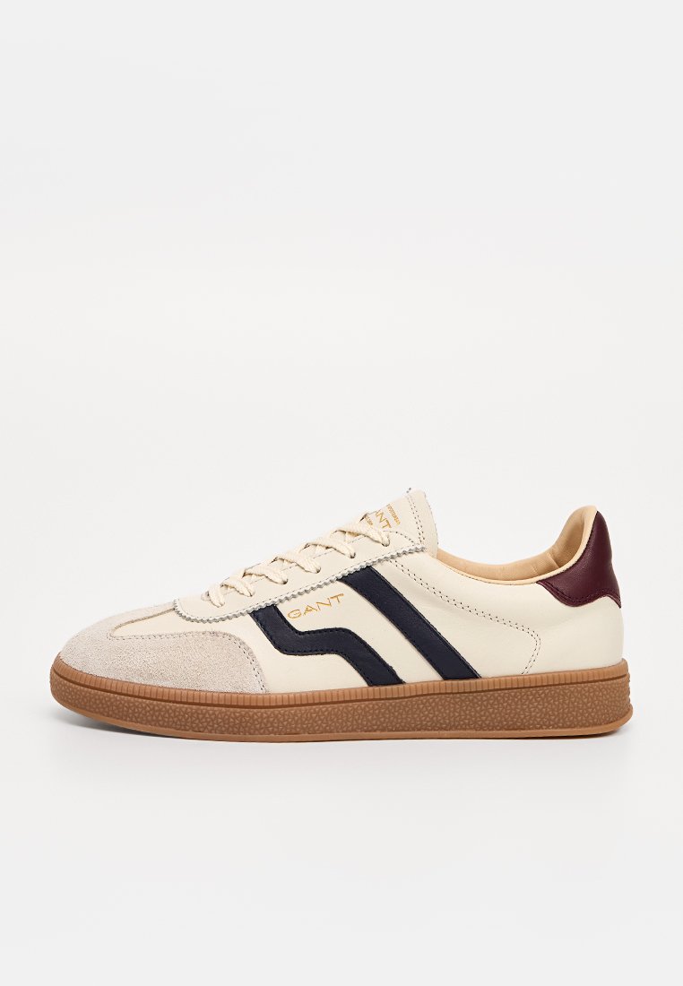 Beige Sneaker aus Wildleder und Leder, mit marineblauen Streifen, einer burgunderfarbenen Ferse und einer strukturierten braunen Gummisohle.