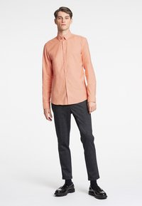 Licht koraalkleurig overhemd met knopen, gemaakt van een gestructureerde stof, in combinatie met donkergrijze slim-fit broeken en zwarte loafers.