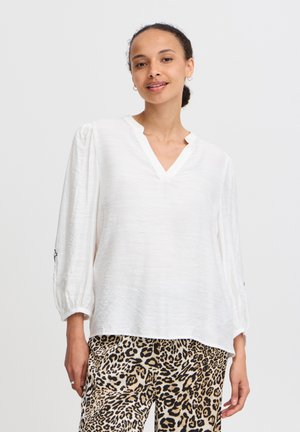Hvid langærmet bluse med V-hals, struktureret stof og rynkede puffærmer. Båret med mønstret leopardprintbukser.