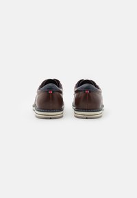 Brown leather shoes with a low profile, navy accents, white sole, and contrasting stitching. Rounded shape with slight padding at the heel.