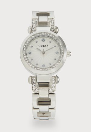 Ceas din oțel inoxidabil argintiu cu un cadran rotund, față albă texturată, accente de cristal și brățară din linkuri. Numele mărcii "Guess" este afișat.