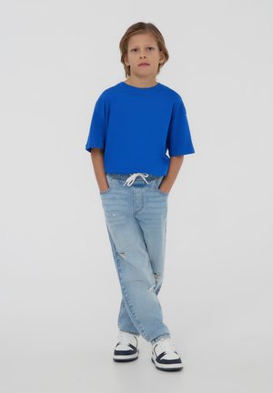 T-shirt corta blu a maniche corte, abbinata a jeans chiari strappati e sneakers bianche con dettagli blu navy.
