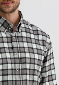 Grijze en witte geblokte flanellen shirt met knoopsluiting, voorzien van een zak, zachte textuur en ronde knopen.