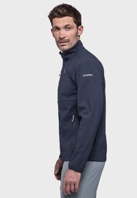 Marineblaue Softshell-Jacke mit hohem Kragen, Reißverschluss-Taschen und elastischen Bündchen, entworfen für Outdoor-Aktivitäten. Glatte Textur, taillierte Form.