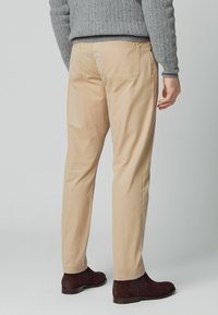 Beige chinos med lige ben, lavet af bomuld. Har to baglommer og bæres med en grå sweater og mørkebrune støvler.