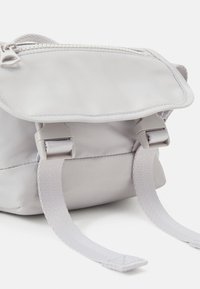 Lille grå nylon rygsæk med klaplukning, justerbar rem og spænde detaljer. Glat tekstur med et minimalistisk design.