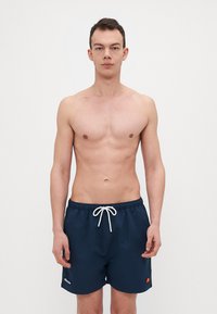 Marineblå svømmebukser laget av lett materiale, med elastisk midjebånd og hvit snøring, samt en liten logo.
