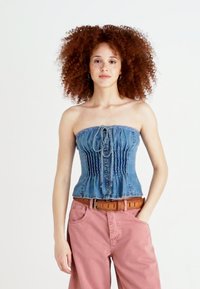 Top de corset sem alças em denim com um Design peplum, apresentando uma textura franzida, frente com cordão e lavagem azul, combinado com calças cor de rosa.