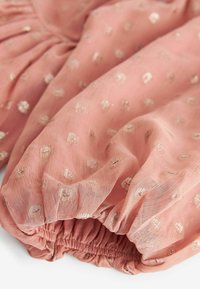 Tissu rose doux et léger avec des points dorés en motif ; ourlet élastiqué froncé ; texture transparente ; tombe en douceur.