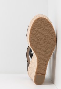 Sandale compensée avec semelle plateforme tissée beige, semelle extérieure en caoutchouc avec motif répété du logo MK et brides en tissu noir.
