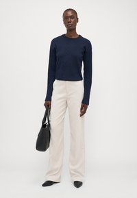 Pull en maille texturée bleu marine à manches longues, associé à un pantalon large crème. Les accessoires incluent un sac fourre-tout noir et des chaussures noires à bout pointu.