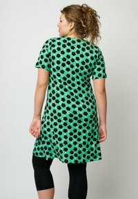 Grön tunika med ett geometriskt svart mönster, kort ärm och avslappnad passform, kombinerad med svarta leggings. Snygg tygtextur.