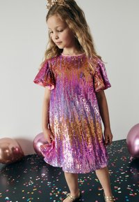 Robe à paillettes scintillantes rose et or avec des manches courtes bouffantes, dotée d'un ourlet évasé. L'arrière-plan comprend des ballons et des confettis colorés.