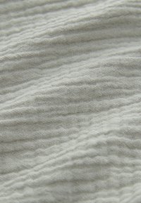 Tessuto grigio chiaro con trama sottile a onde, realizzato in materiale leggero e traspirante, che offre un aspetto morbido e leggermente stropicciato.