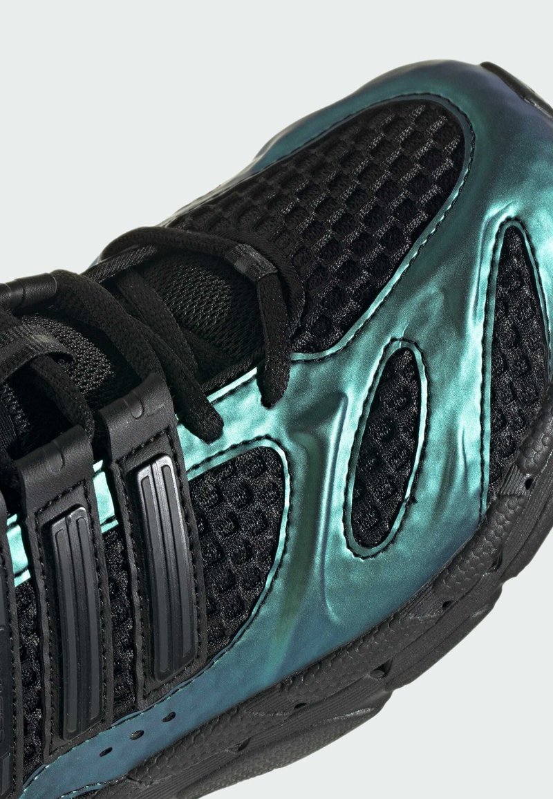 Sort mesh sneaker med metallisk teal overlays, sorte snørebånd og tre sorte teksturerede remme på siden, vist i nærbillede.