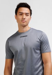 Gray athletic shirt made of smooth, moisture-wicking fabric. Features short sleeves and a round neckline with "HUMMEL" logo on front.